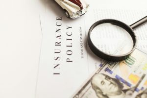 insurance policy document, a dollar bill, a magnifying glass, and a model muscle car